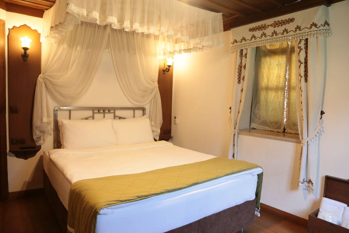 A neatly made bed with a green blanket, a canopy, and wall-mounted lamps.