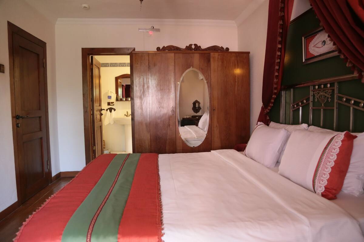 A bedroom with a large bed, a wooden wardrobe, and a mirror.