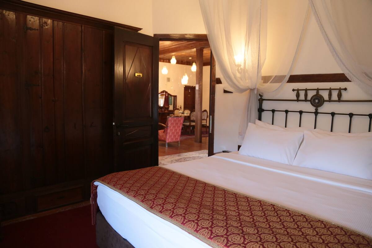 A bedroom with a bed, a wooden wardrobe, and a door leading to another room.