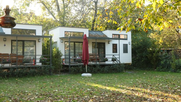 Una casa moderna con terraza y mobiliario exterior, rodeada de jardín y árboles.