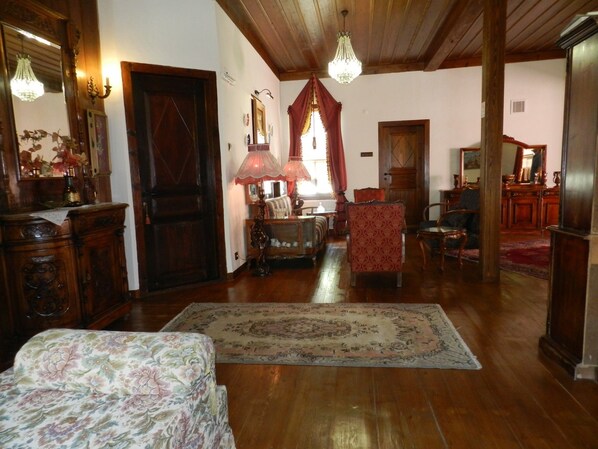 A spacious living room with wooden floors, a large rug, a sofa, a chair, and a wooden cabinet.