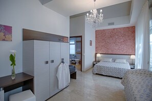 Une chambre d’hôtel dotée d’une grande armoire, d’un lit recouvert d’une couvre-lit à motifs floraux, d’un lustre et donnant sur la salle de bain.