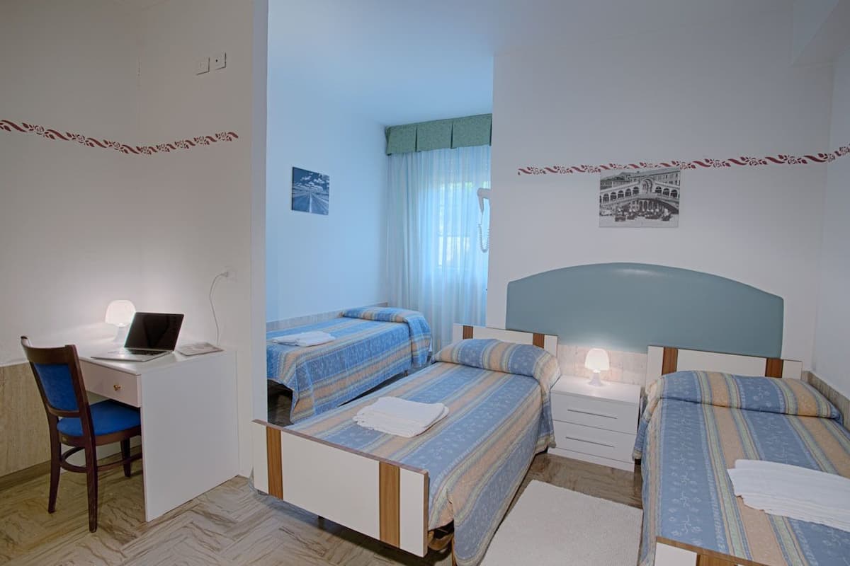 A bedroom with two single beds, a desk with a laptop, and a chair.