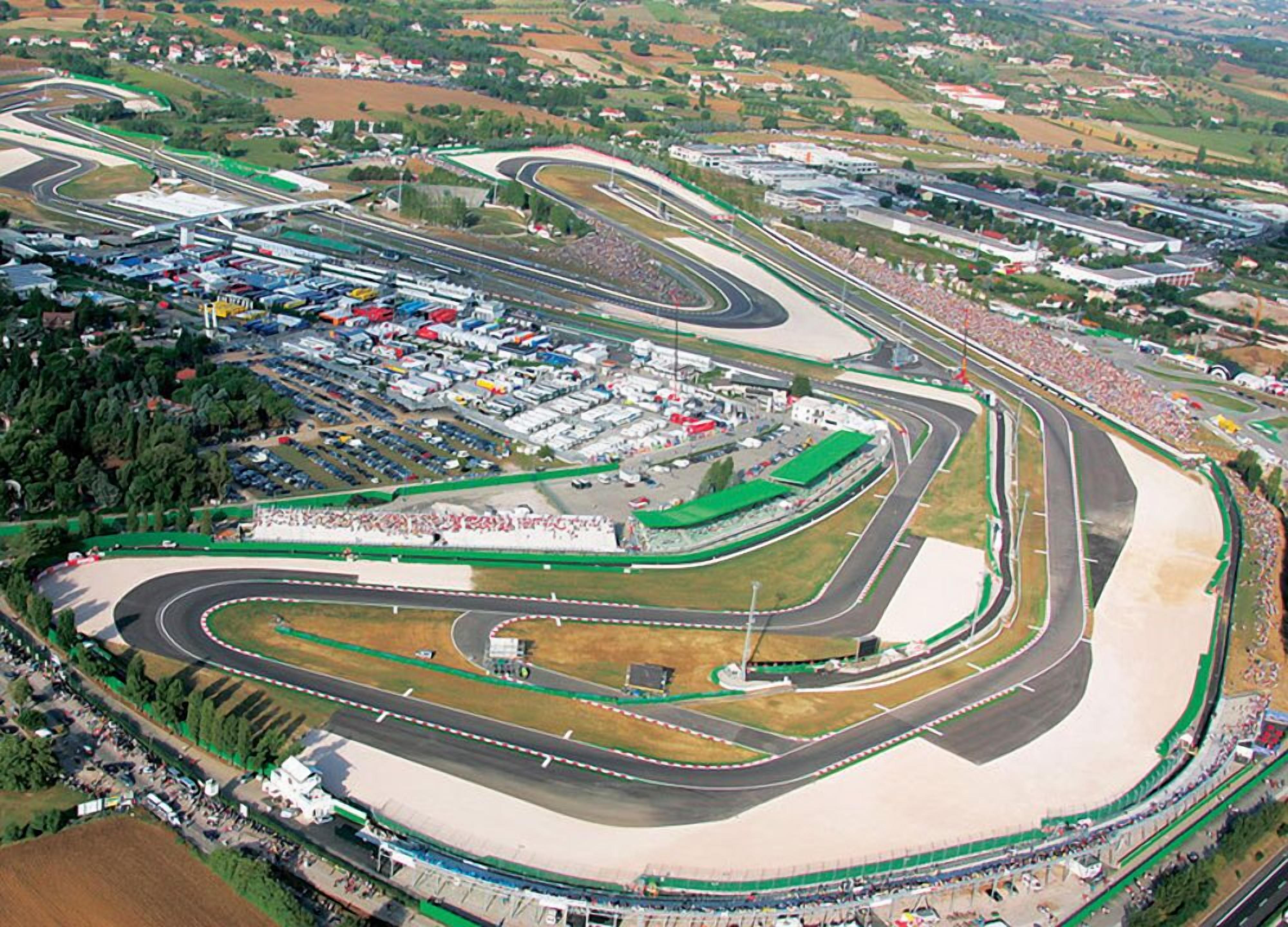 Vue aérienne d’un circuit automobile comportant plusieurs pistes, des tribunes pour les spectateurs et un parking.