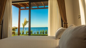 A bedroom with a large bed, a view of the sea, and curtains on the windows. - Home The Residence (Nosy Be)