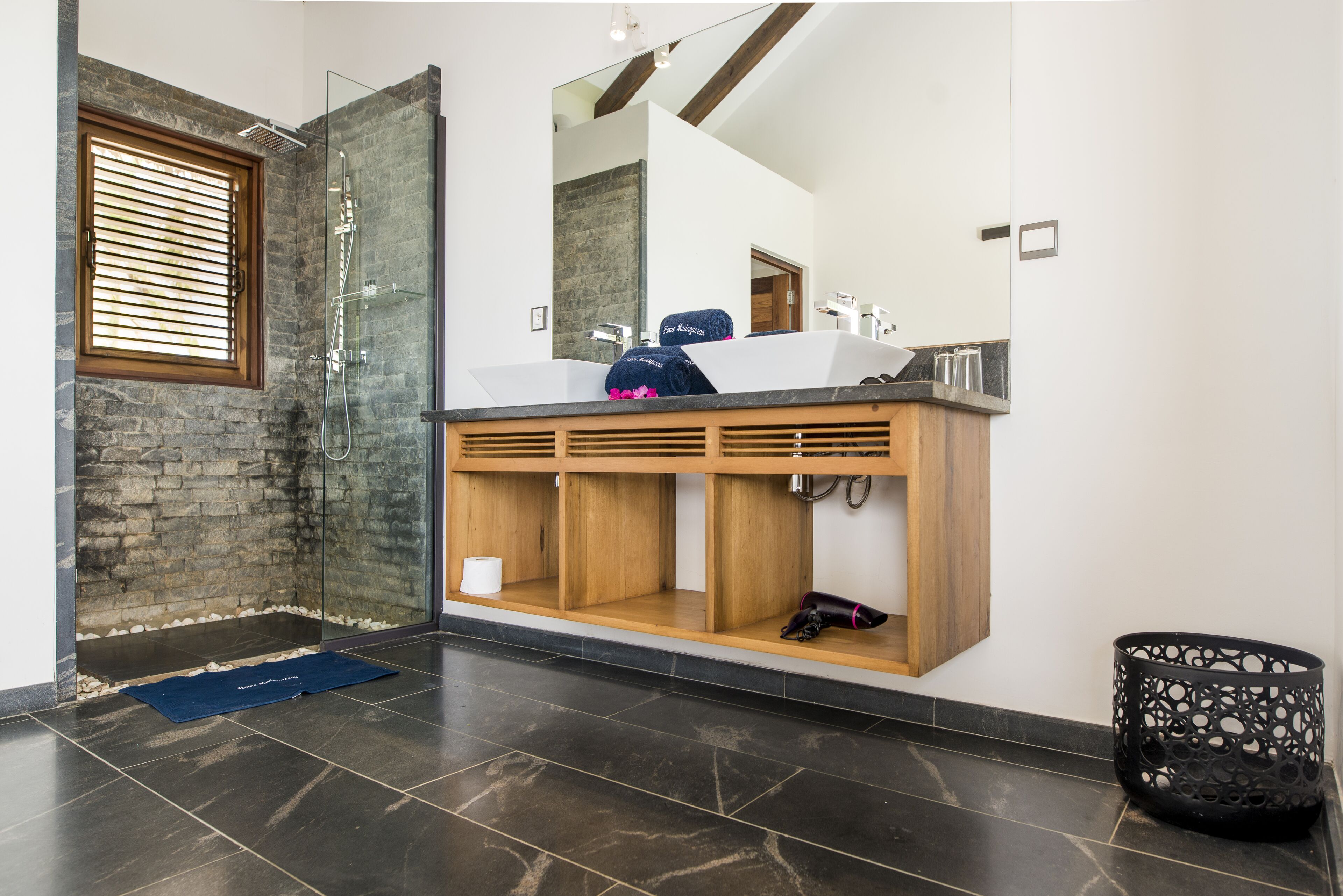 A modern bathroom with a stone wall, a glass shower enclosure, a wooden vanity with a sink, and a large mirror.