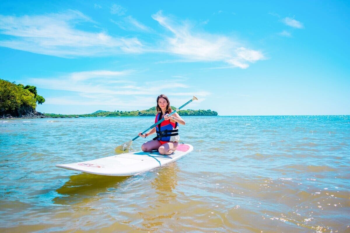Una persona seduta su una tavola da paddleboard in acque calme, con cielo sereno e terra all'orizzonte.