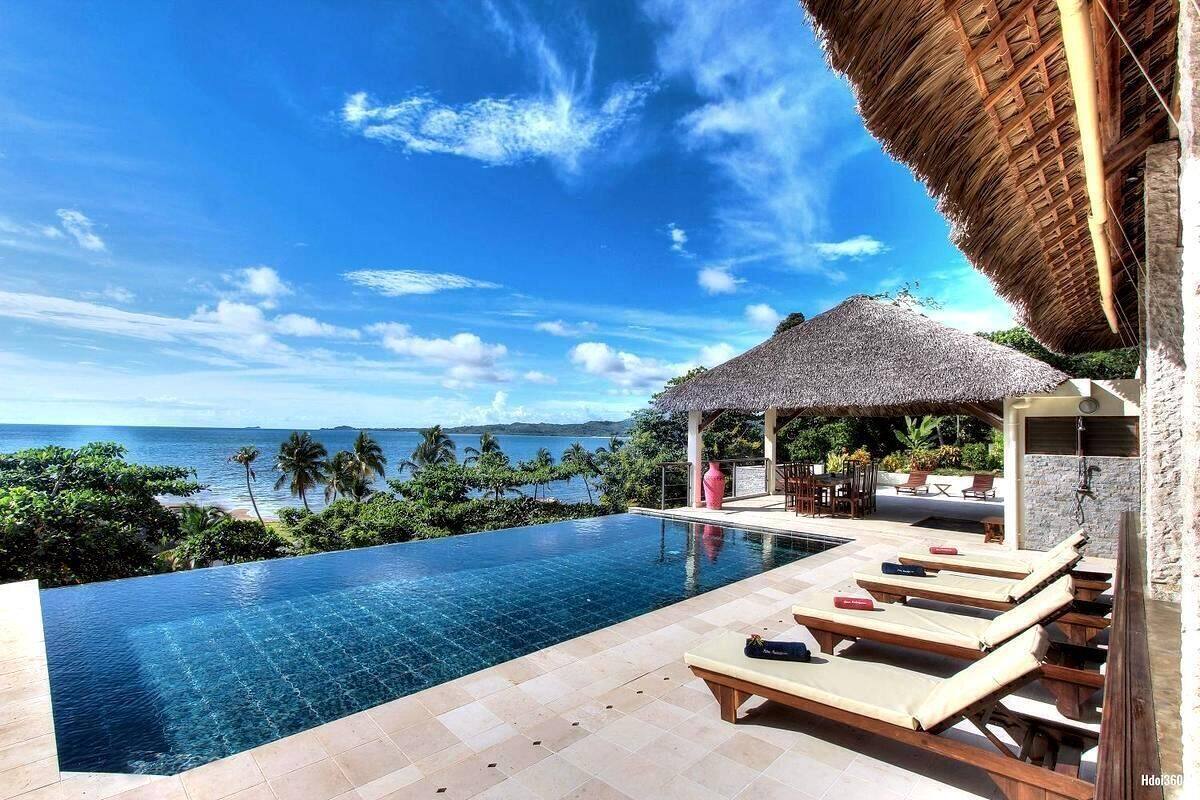 A infinity pool with a view of the ocean, lounge chairs, and a thatched-roof structure.