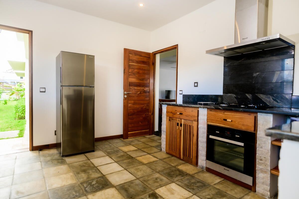 A kitchen with a stainless steel refrigerator, wooden cabinets, a built-in oven, and a black countertop.