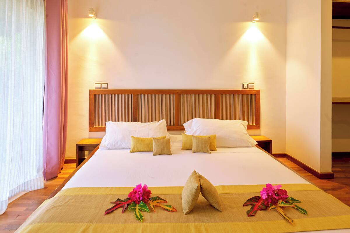 A hotel room with a large bed, two bedside tables, a wooden headboard, and two wall-mounted lights.