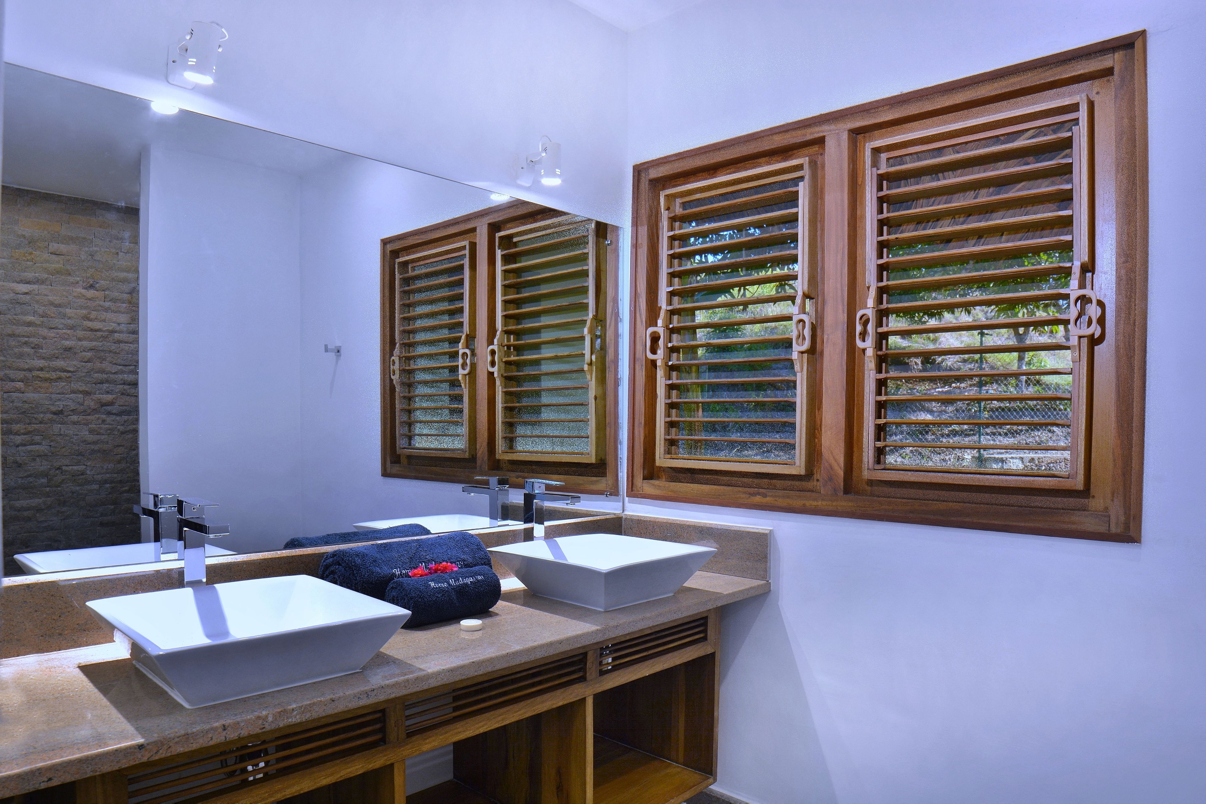 Un baño con dos lavamanos, un espejo y persianas de madera.