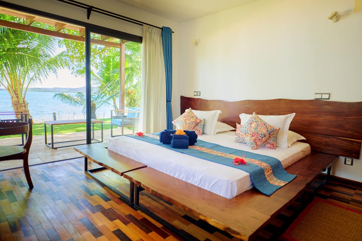 A bedroom with a large bed, a bench, and a view of the sea.
