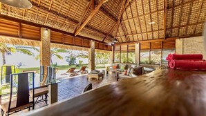 An indoor area with a thatched roof, wooden furniture, and a view of palm trees outside. - Home The Residence (Nosy Be)