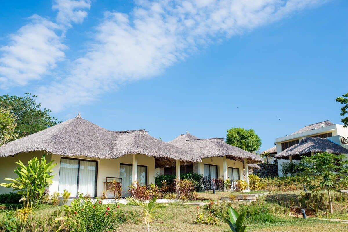 A resort with thatched-roof cottages, a well-maintained garden, and a clear blue sky.