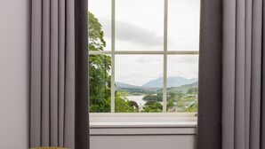 A room with a view of a landscape through a window, a yellow armchair, and a small table with a book. - The Marmalade Hotel (Portree)