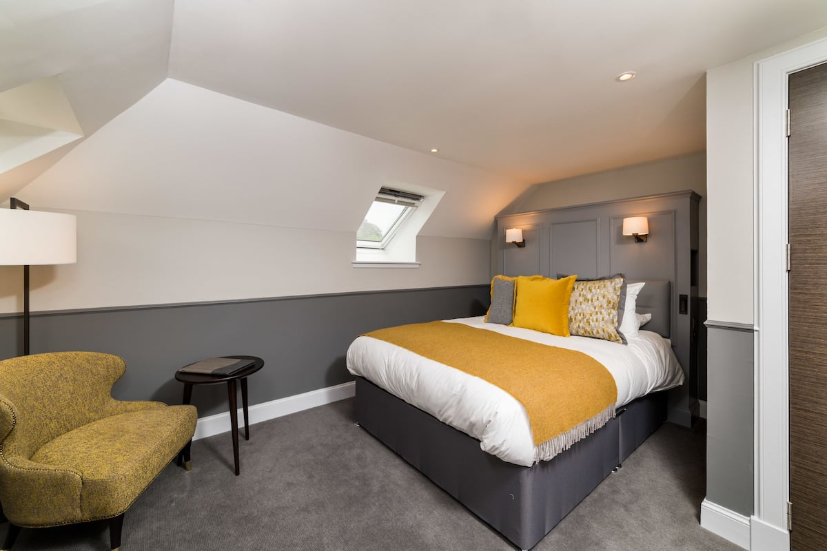 A bedroom with a bed, a chair, a small table, a window, and a door.