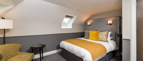 A bedroom with a bed, a chair, a small table, and a skylight.