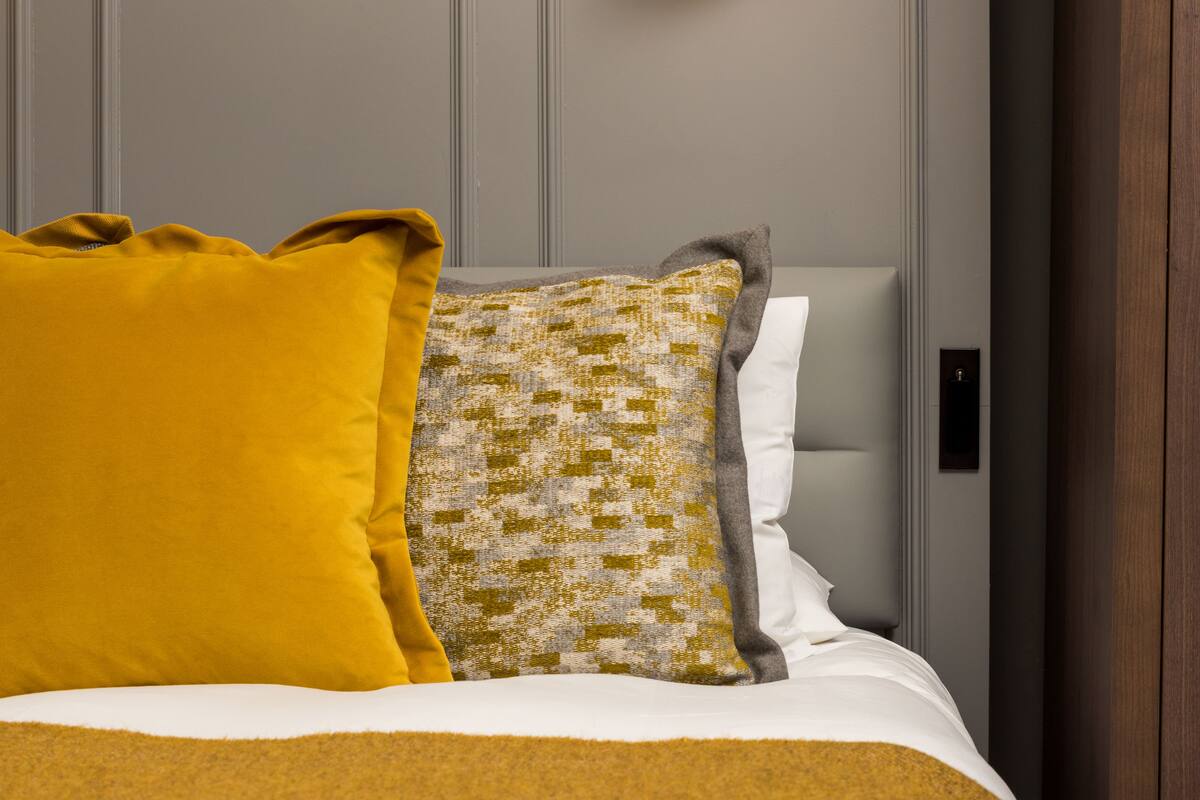 A bed with a mustard-colored blanket, a patterned pillow, and a white pillow.