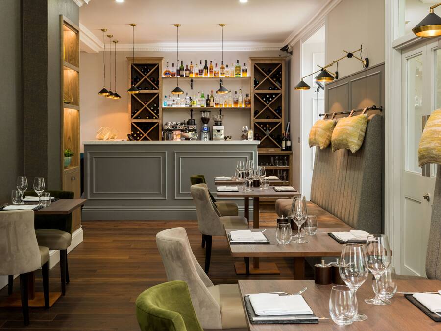 A restaurant with a bar area, wooden furniture, and wine bottles on shelves.