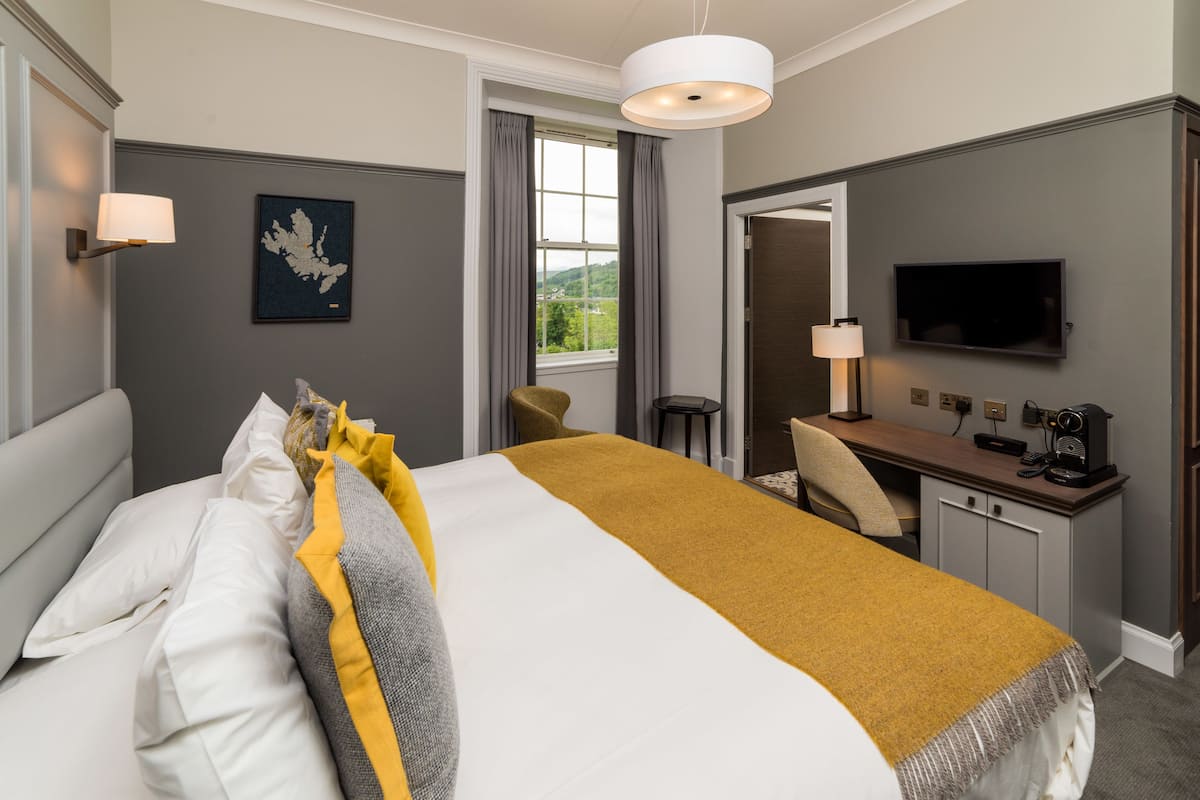 A hotel room with a bed, a desk, a television, and a window with curtains.