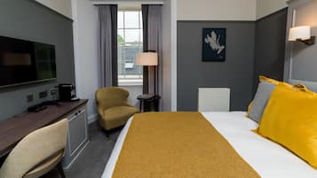 Habitación de hotel con cama, escritorio, silla, televisor y ventana con cortinas.