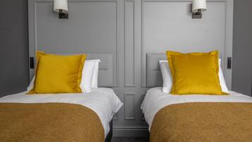 A hotel room with two beds, each with a white and yellow pillow, and a brown blanket. There are two wall-mounted lamps on either side of the door.