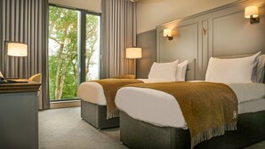 A hotel room with two beds, a desk, and a view of trees through large windows. - The Marmalade Hotel (Portree)