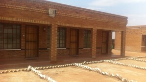 A brick building with multiple doors and windows, a paved area with a stone border, and a clear sky. - Jeara Guest House (Serule)