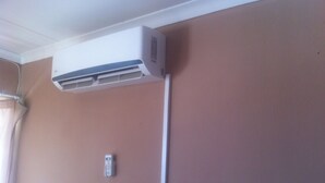 A wall-mounted air conditioning unit with a remote control on the wall. - Jeara Guest House (Serule)