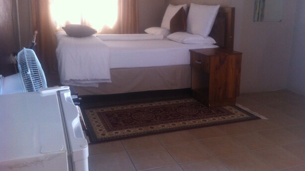 A bedroom with a bed, a bedside table, a fan, and a window with curtains. - Jeara Guest House (Serule)