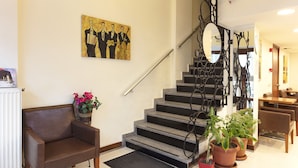 Una escalera con barandilla metálica, un sofá de cuero marrón, una planta en maceta y un cuadro en la pared.