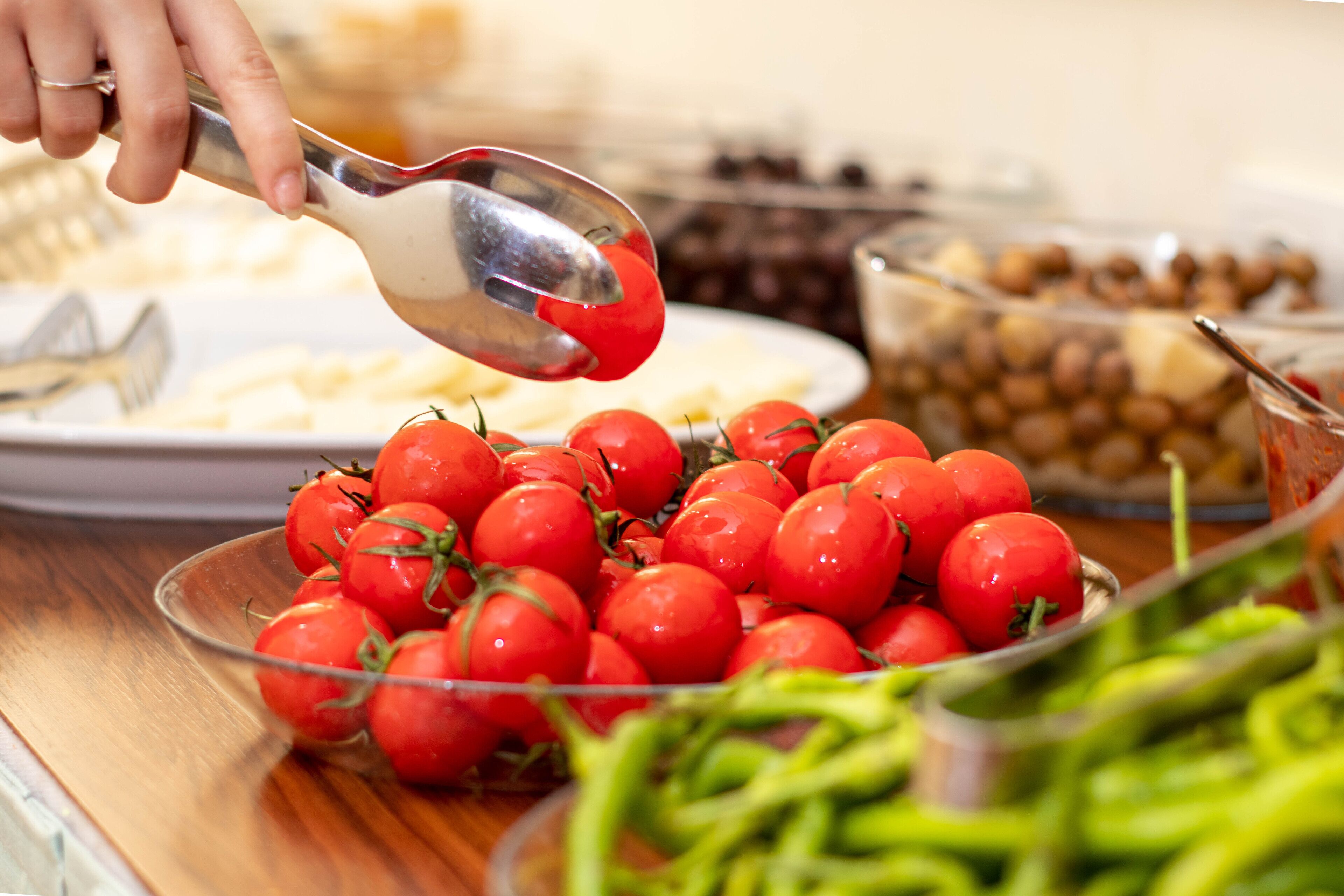 A buffet with various food items including a bowl of cherry tomatoes, a plate of cheese, and a bowl of olives.