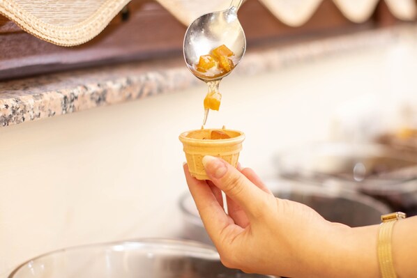 Una mano sosteniendo un cono de waffle al que se está sirviendo mielada con una cuchara.