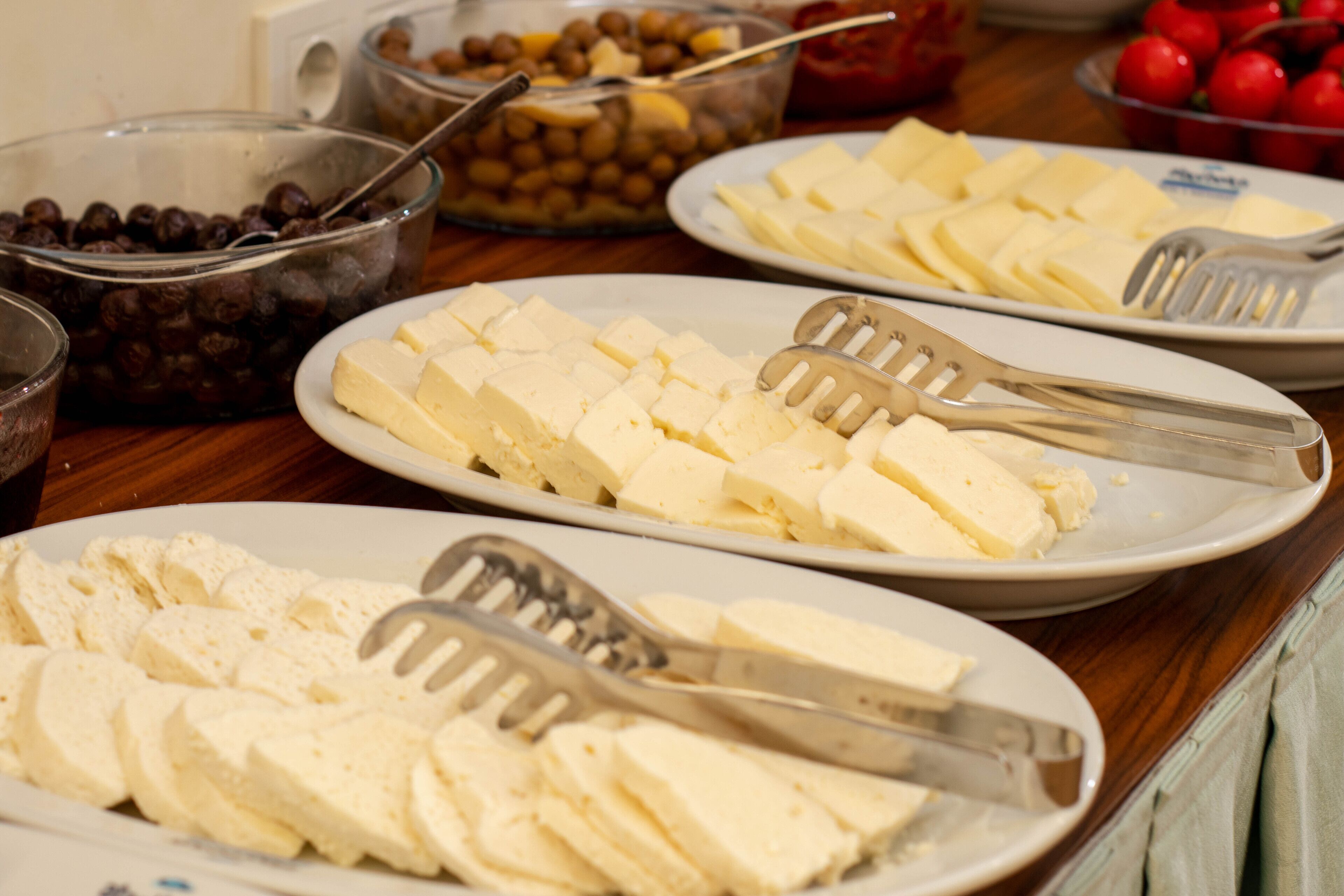 A buffet table with various food items including cheese, olives, and tomatoes.