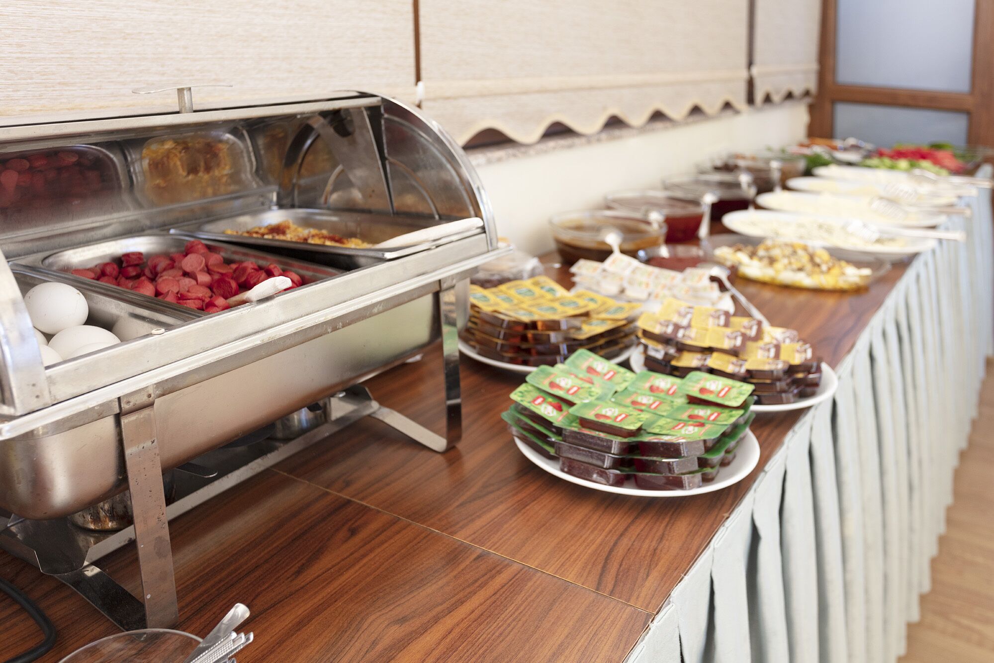 Un buffet con diversi alimenti, tra cui uova, salsicce e dolci confezionati.