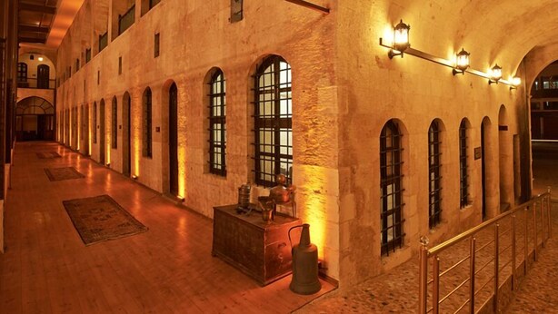 A spacious corridor with arched windows and a wooden floor, featuring a central wooden bench and a vintage-style lamp. - Sirehan Hotel (Gaziantep)