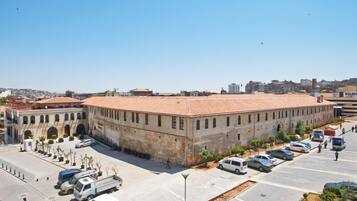 Un edificio grande e histórico con techo plano y ventanas arqueadas, rodeado por un estacionamiento con varios vehículos.