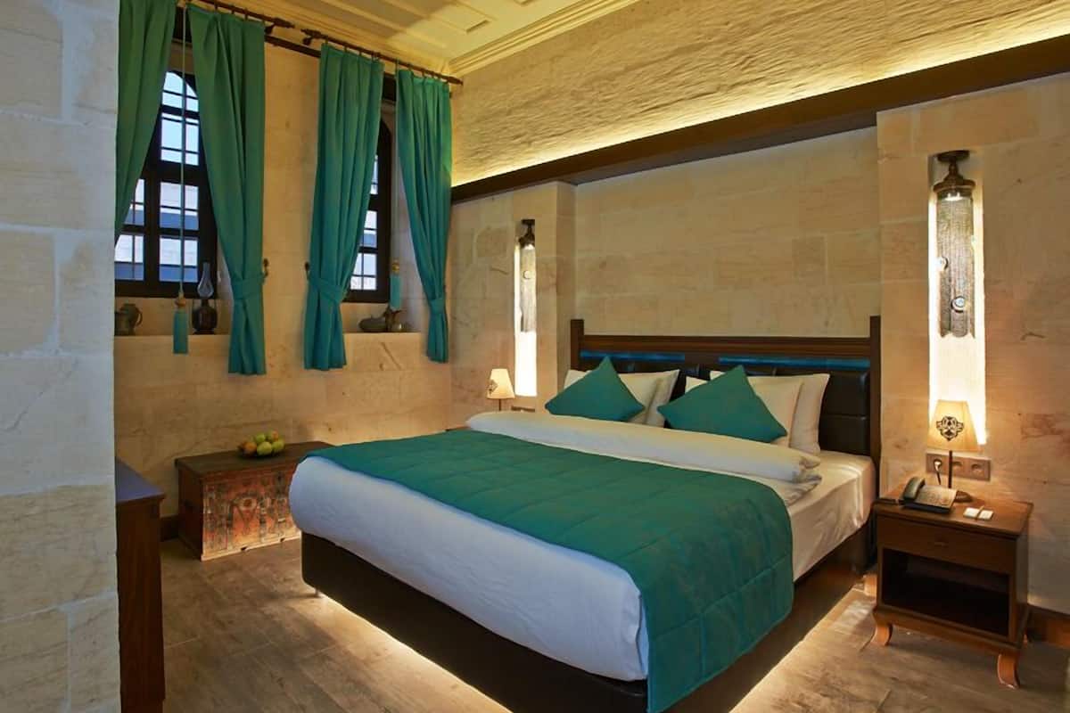 Ein geräumiges Schlafzimmer mit einem großen Bett, einem Holz-Kopfende und einer Steinwand. Zwei Nachttische mit Lampen und ein kleiner Tisch mit Obst sind ebenfalls vorhanden.