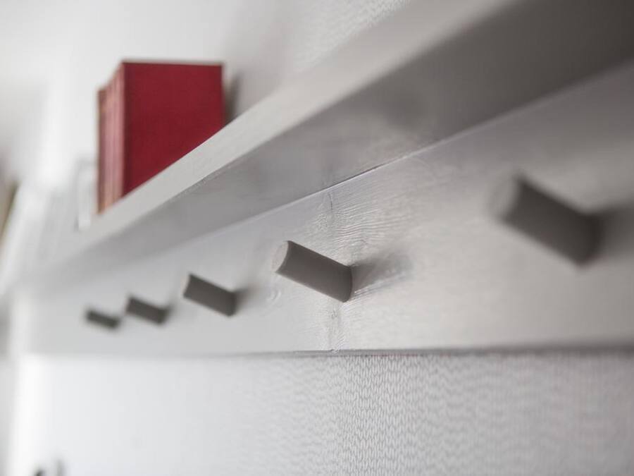 Close-up de uma parede branca com uma estante contendo vários livros e um livro vermelho.
