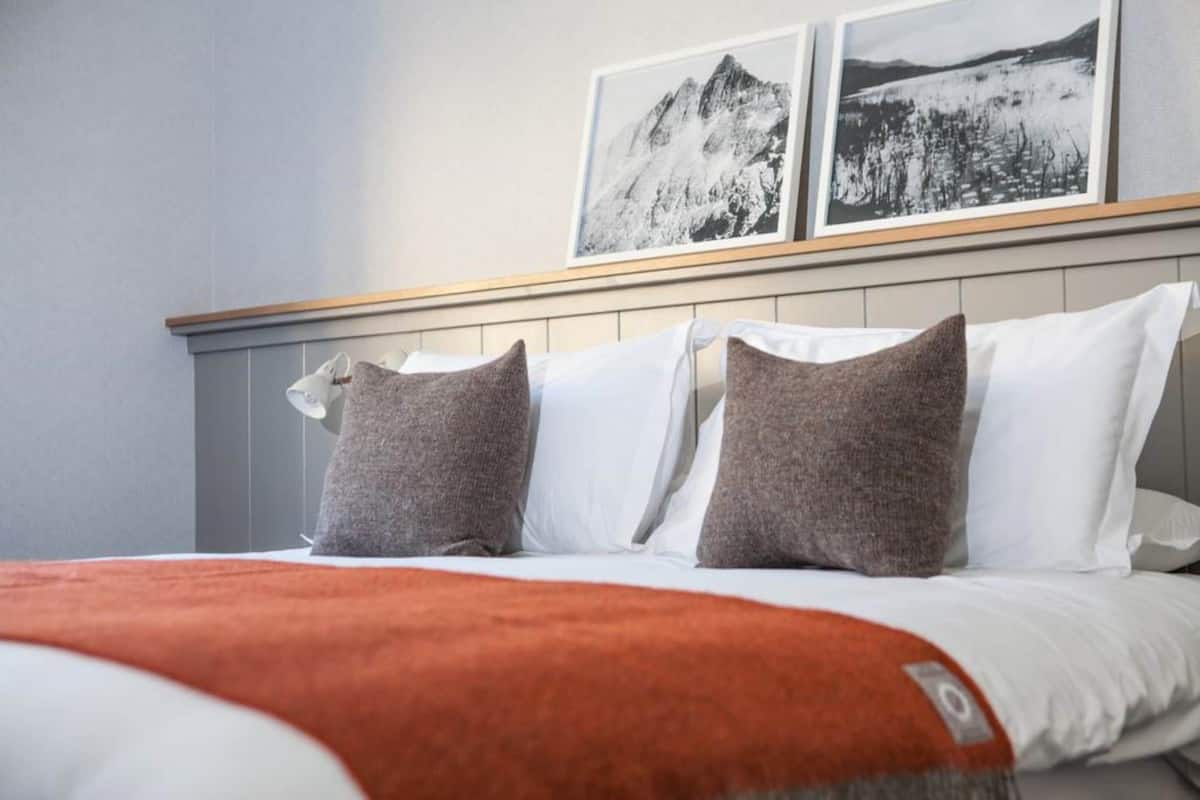 A hotel room with a bed, pillows, a blanket, and two framed pictures on the wall.