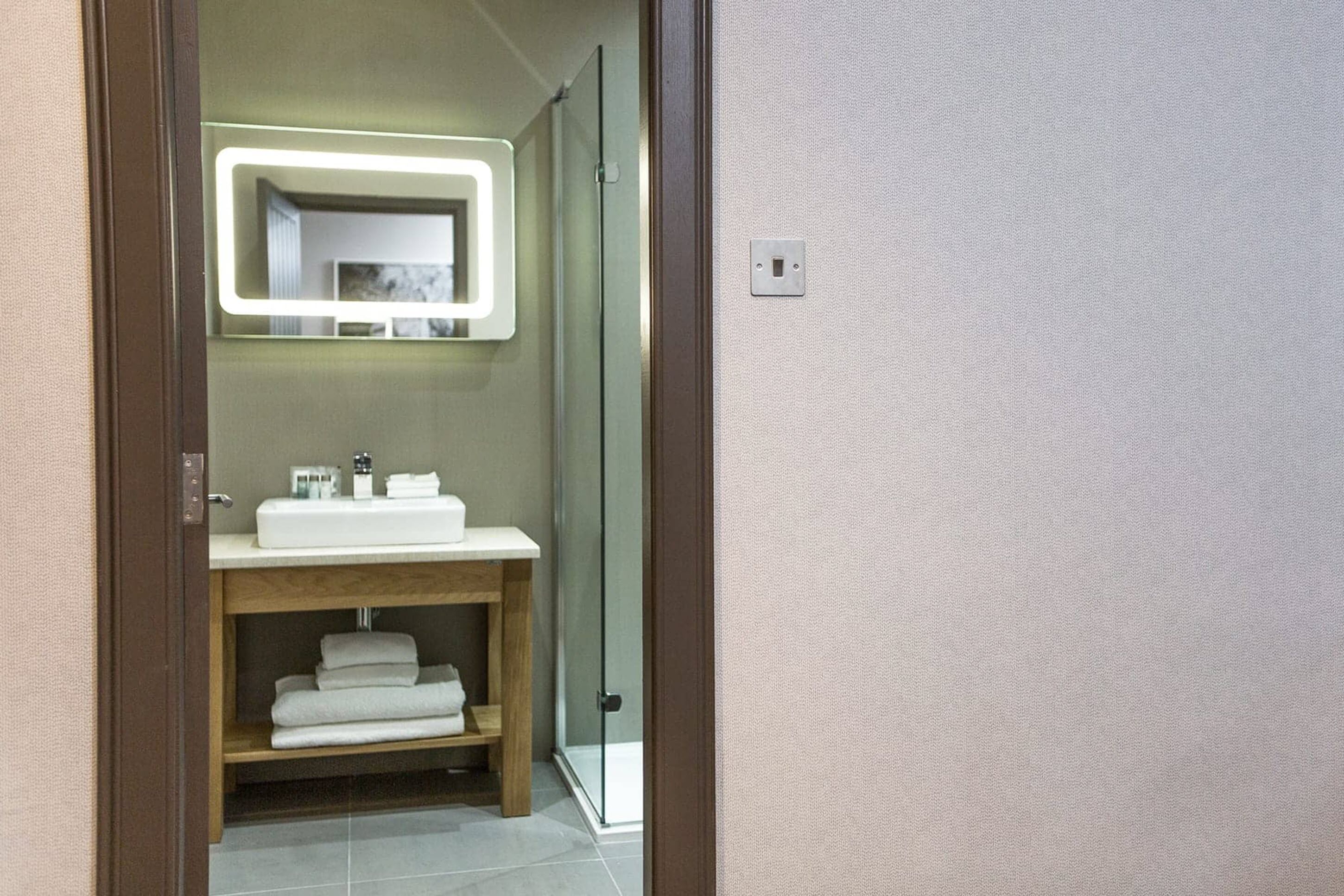 A modern bathroom with a white sink, a mirror with LED lighting, and a glass shower door.