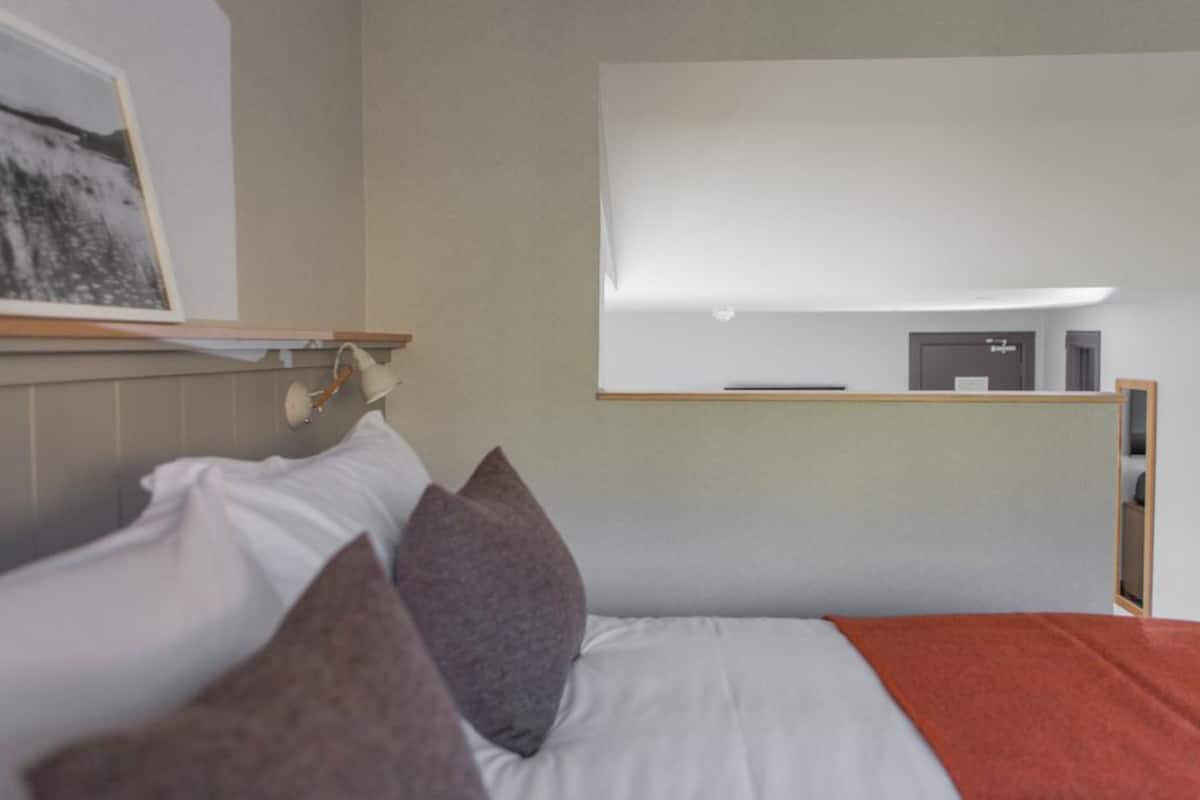 A modern hotel room with a bed, pillows, a bedside table, and a wall-mounted TV.