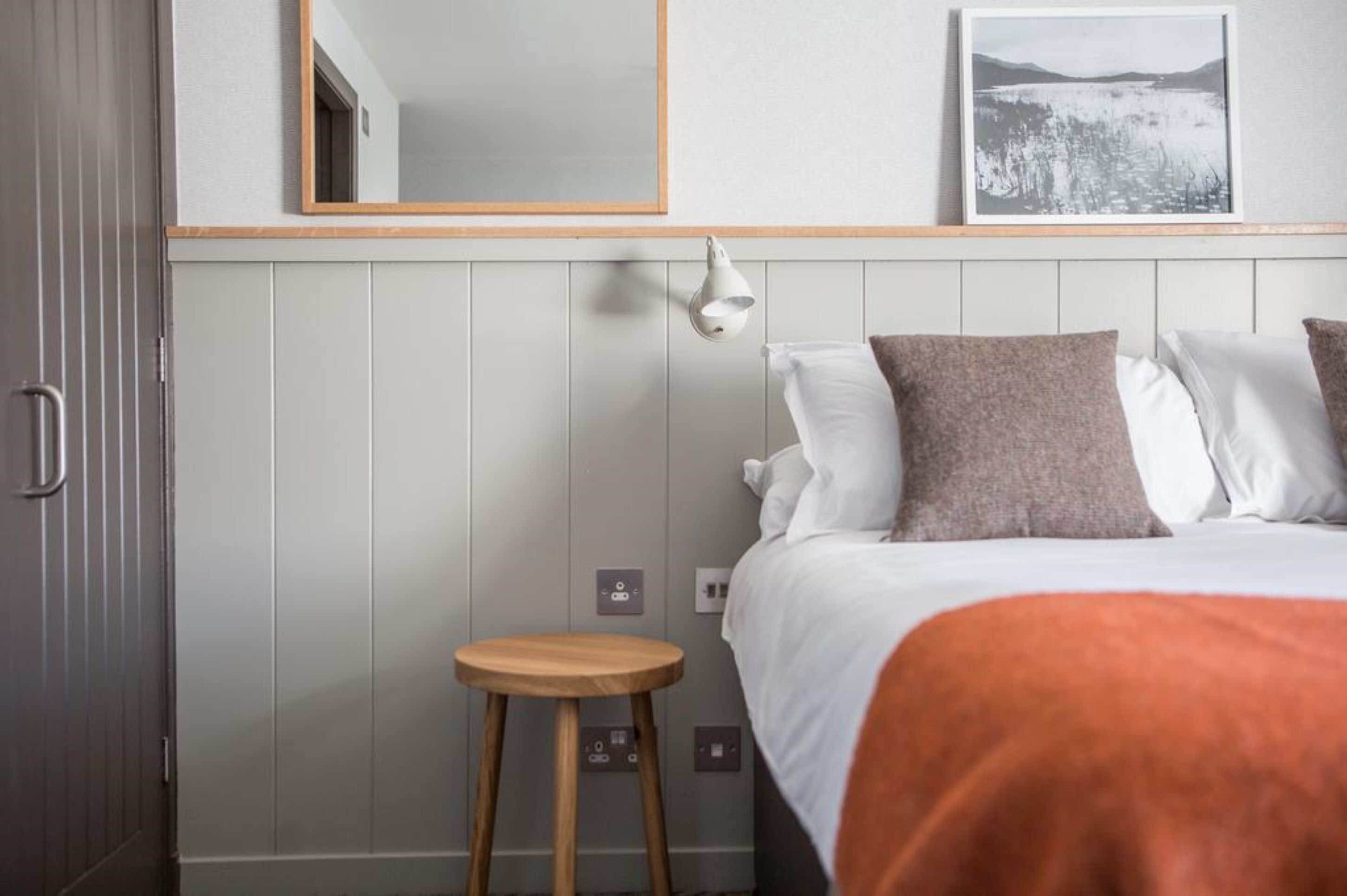 Ein Hotelzimmer mit einem Bett, einem kleinen Hocker, einer Wandleuchte und einem gerahmten Bild.