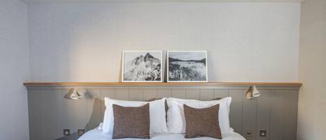 A hotel room with a bed, two pillows, a red blanket, a wooden headboard, two wall-mounted lamps, and two framed pictures on the wall.
