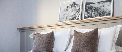 A hotel room with a bed, pillows, and two framed pictures on the wall.