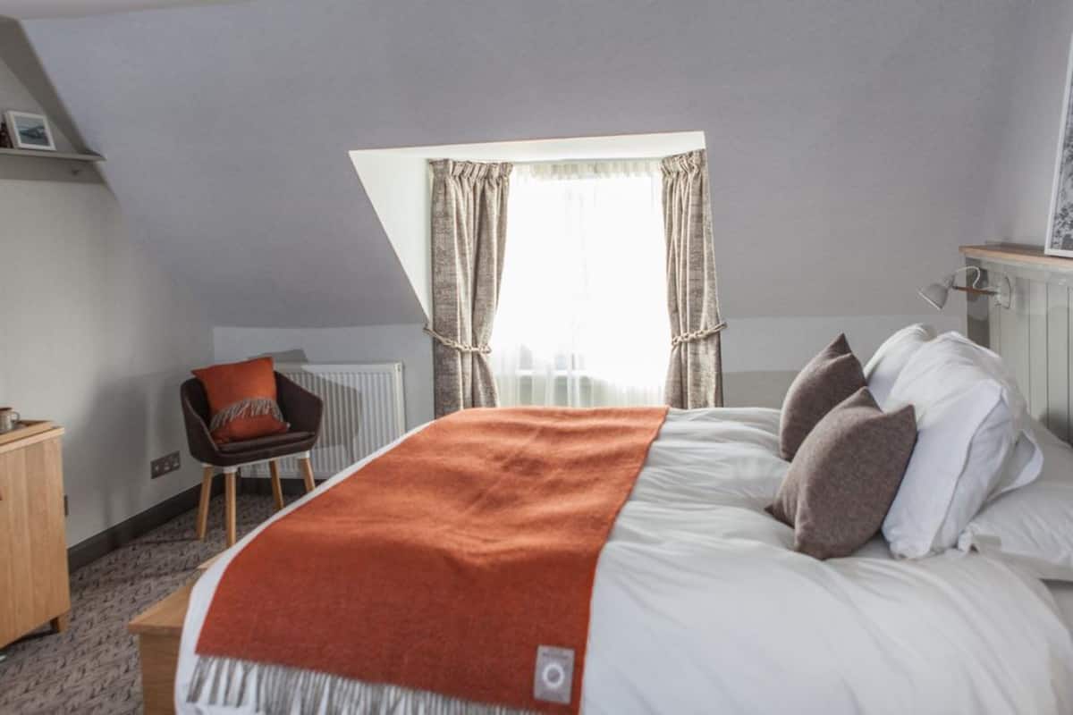 A bedroom with a bed, a chair, a radiator, and a window with curtains.