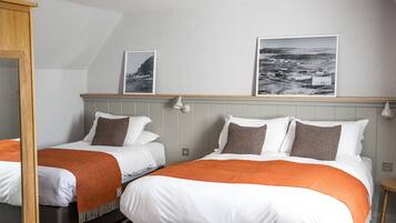 A hotel room with two beds, each with white bedding and orange throw blankets. There are two framed pictures on the wall above the beds.