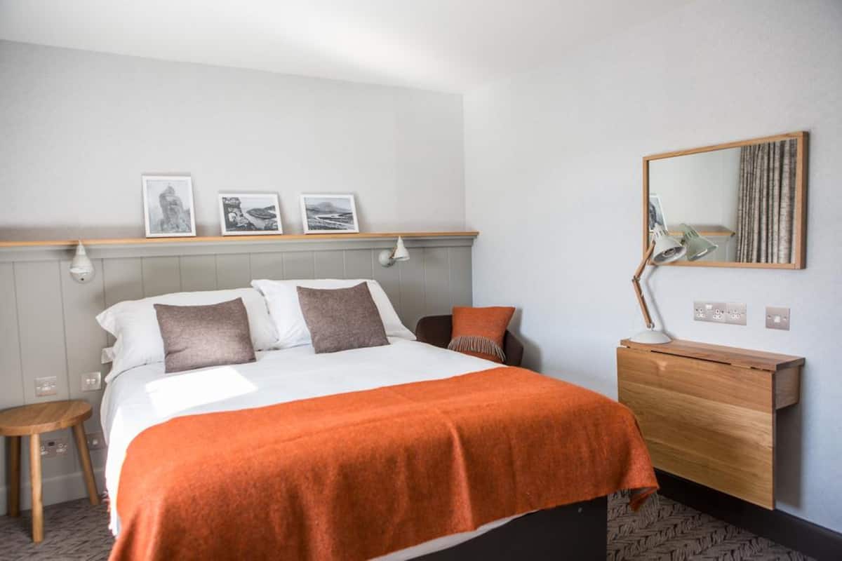 A hotel room with a bed, a wooden nightstand, a mirror, and framed pictures on the wall.