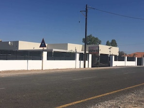 A road with a triangular warning sign, a building with a gated entrance, and a clear sky. - Eagle Suites Guest House (Ghanzi)