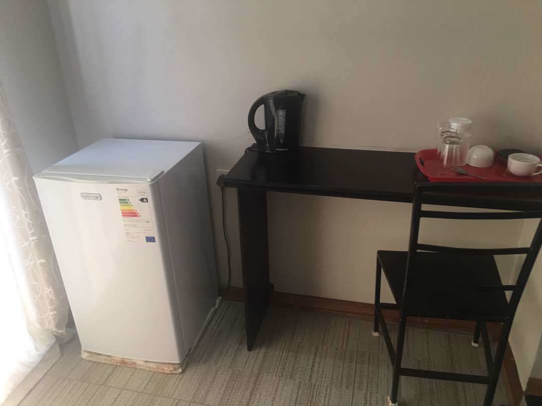 Una kitchenette compacta con refrigerador, cafetera, una mesita con una silla y una bandeja roja.
